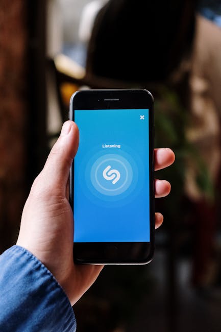 Close-up of a hand holding a smartphone displaying a music listening app interface.